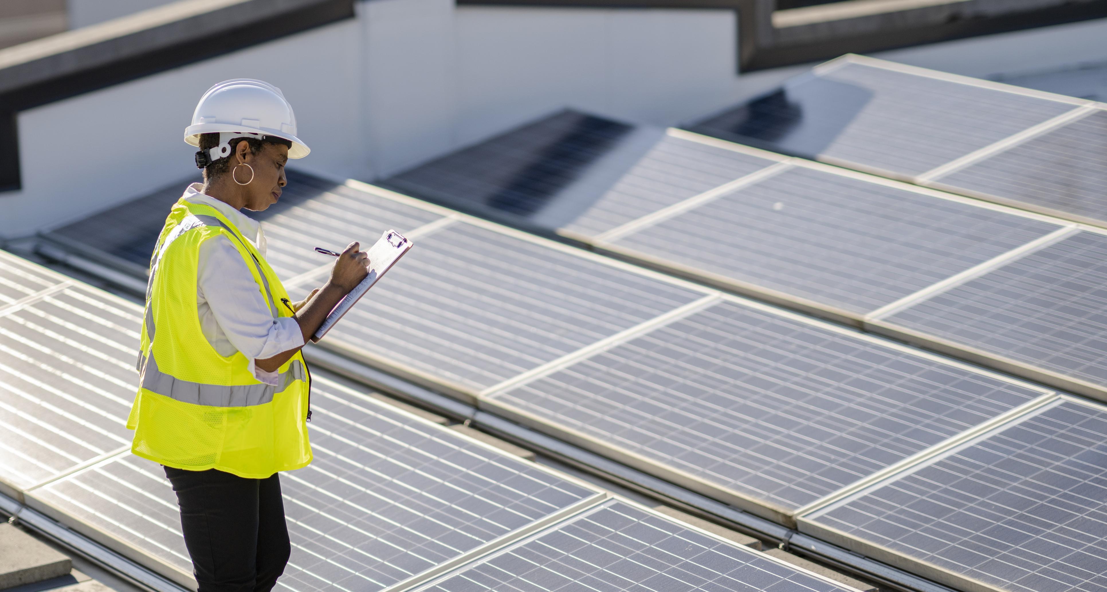 Une femme examine des panneaux solaires sur un toit pour en vérifier l’efficacité et le bon fonctionnement.