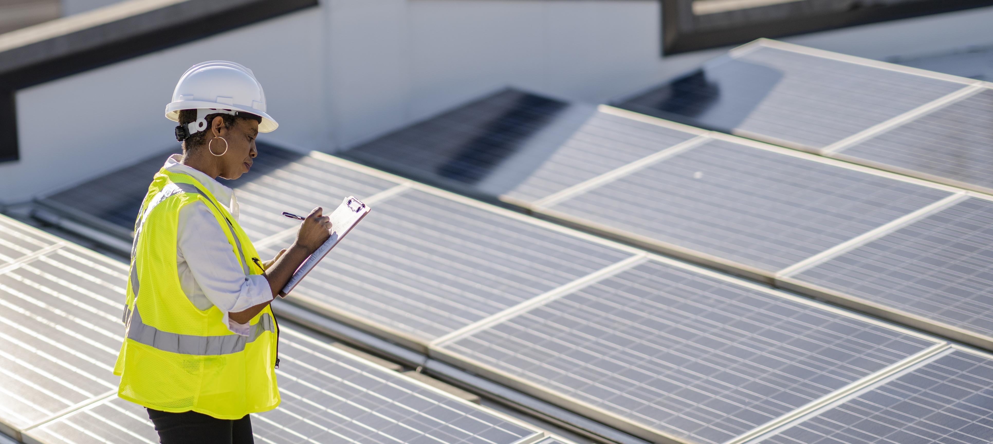 Une femme examine des panneaux solaires sur un toit pour en vérifier l’efficacité et le bon fonctionnement.