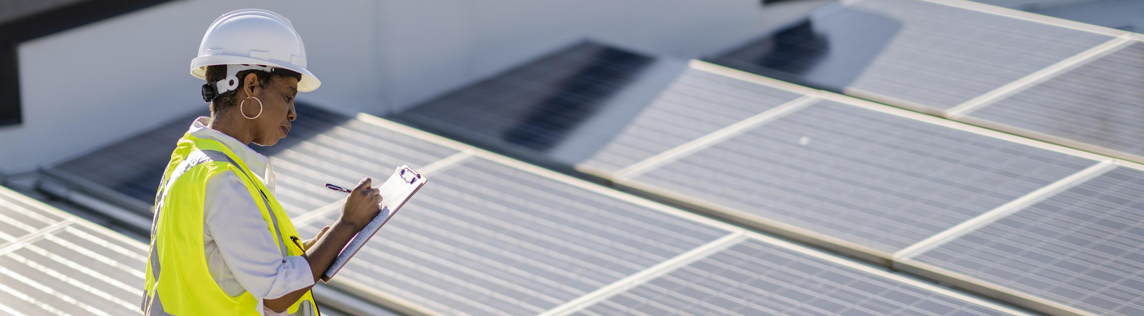 Une femme examine des panneaux solaires sur un toit pour en vérifier l’efficacité et le bon fonctionnement.