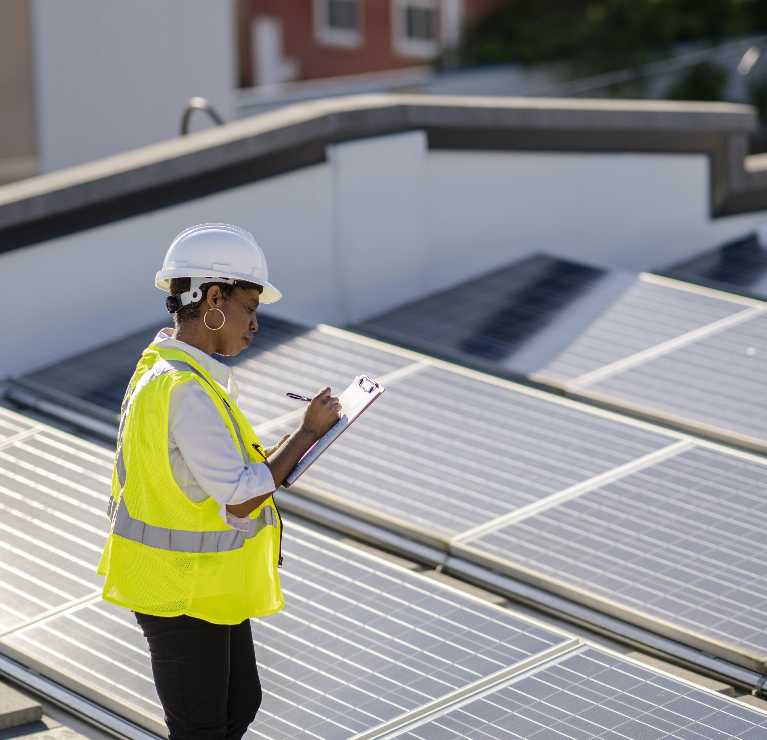 Une femme examine des panneaux solaires sur un toit pour en vérifier l’efficacité et le bon fonctionnement.